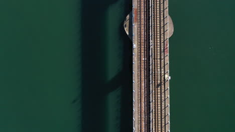 An-aerial-shot-over-train-tracks-over-a-bay-with-green-water-on-a-sunny-day