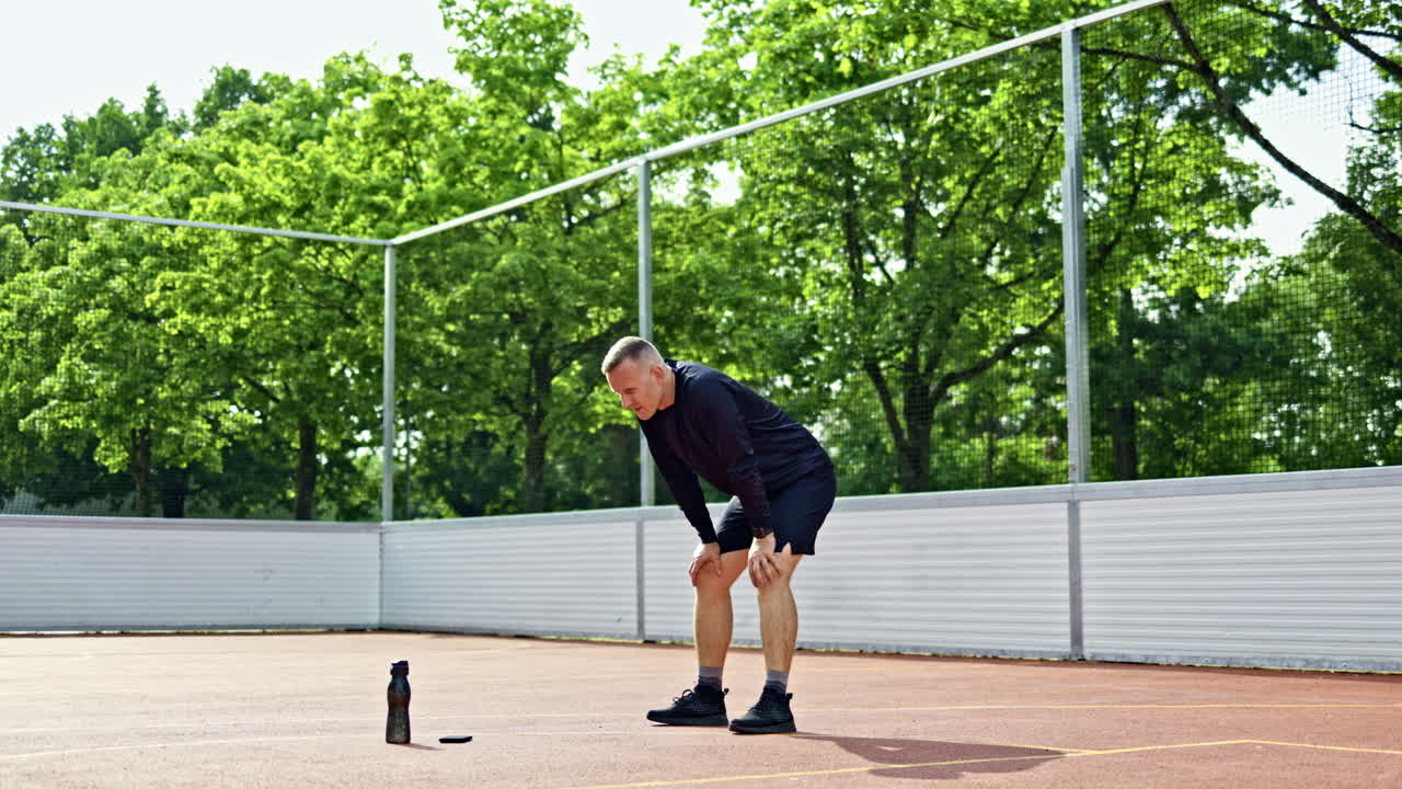 A handsome man in shorts and a T-shirt is training on a sports ground in the park. A man is training outdoors. A sports lifestyle