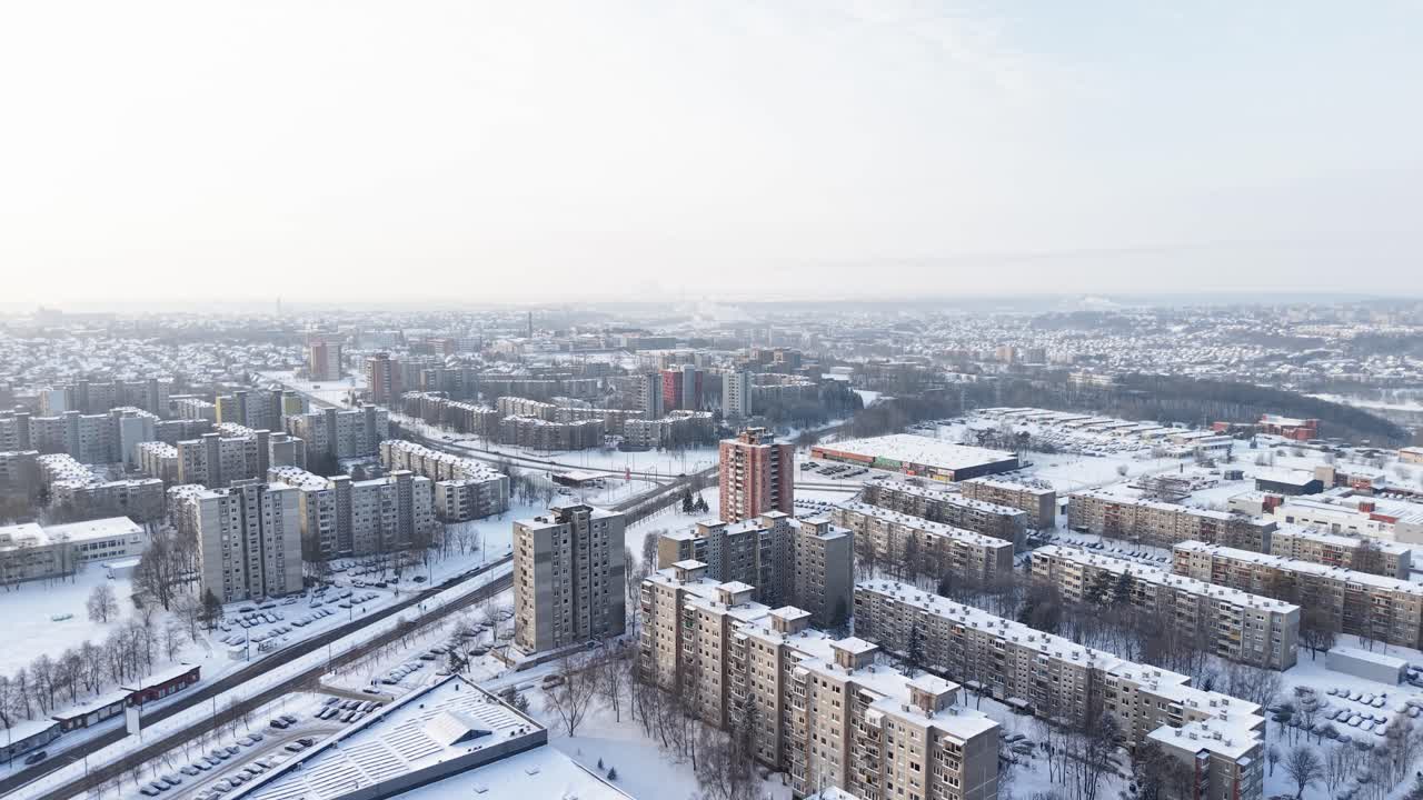 Ein Drohnenvideo bietet eine umfassende Luftaufnahme einer schneebedeckten Stadtlandschaft mit zahlreichen Hochhäusern. Die Winterszene erzeugt eine heitere und doch geschäftige Atmosphäre in der Stadt.