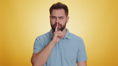 young bearded man presses finger to lips makes silence gesture sign do not tells secret stop gossip