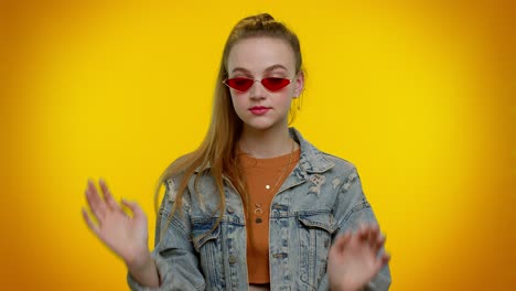 Seductive-cheerful-stylish-girl-in-denim-jacket-wearing-sunglasses,-charming-smile-on-yellow-wall