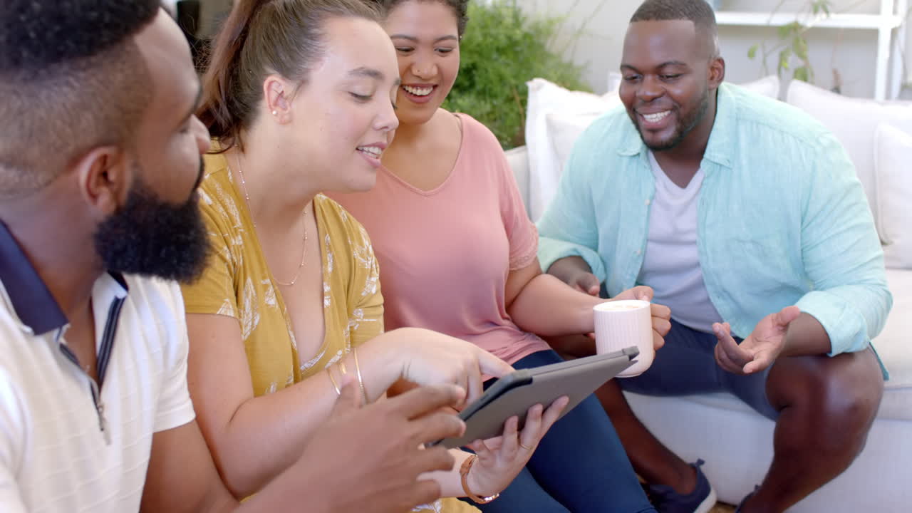 diverse friends sitting together, using tablet and drinking coffee, enjoying time at home