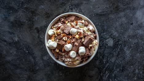 primer plano de un tazón de helado de chocolate con malvaviscos, almendras y salsa de chocolate