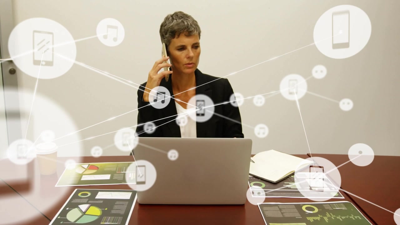 En kvinde taler i sin mobiltelefon ved sit skrivebord på et kontor