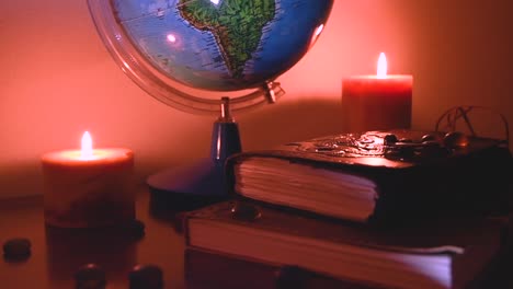 globe in flickering candles light background on a wooden surface with stones and ancient books