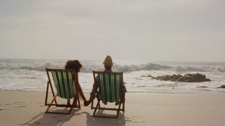 Vista posteriore di una coppia afroamericana che si rilassa insieme su un lettino prendisole in spiaggia 4k