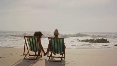 Rear-view-of-African-American-couple-relaxing-together-on-a-sun-lounger-at-beach-4k