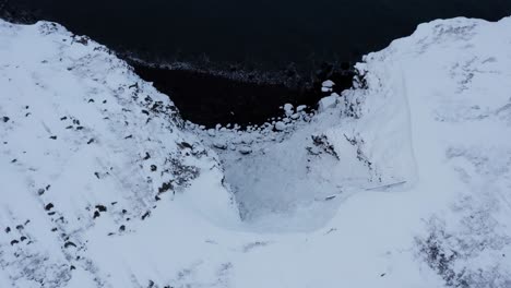 steep rocky cliffs covered in snow during winter time, iceland, aerial