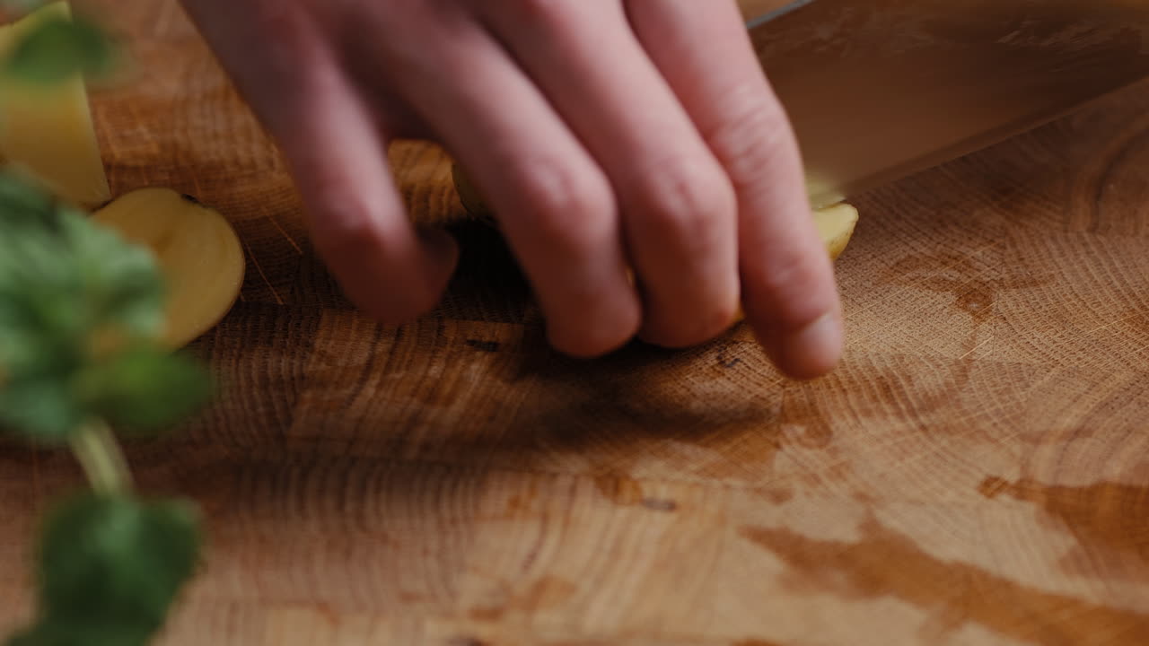 Male chef sliceing potato in the kitchen on a wooden cutting board in the kitchen
