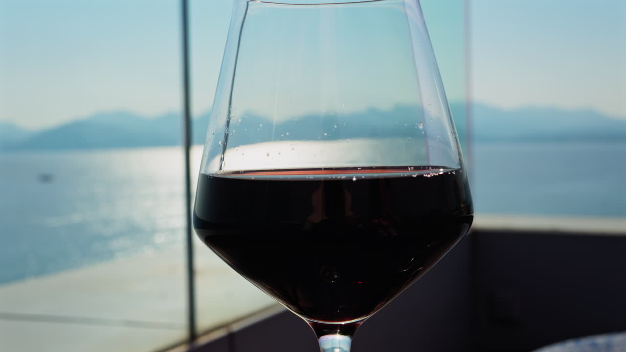 Close up of a glass of red wine on a table at a terrace with a sea view