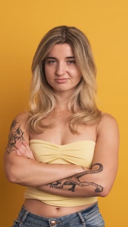 unhappy young woman standing with crossed hands on yellow background