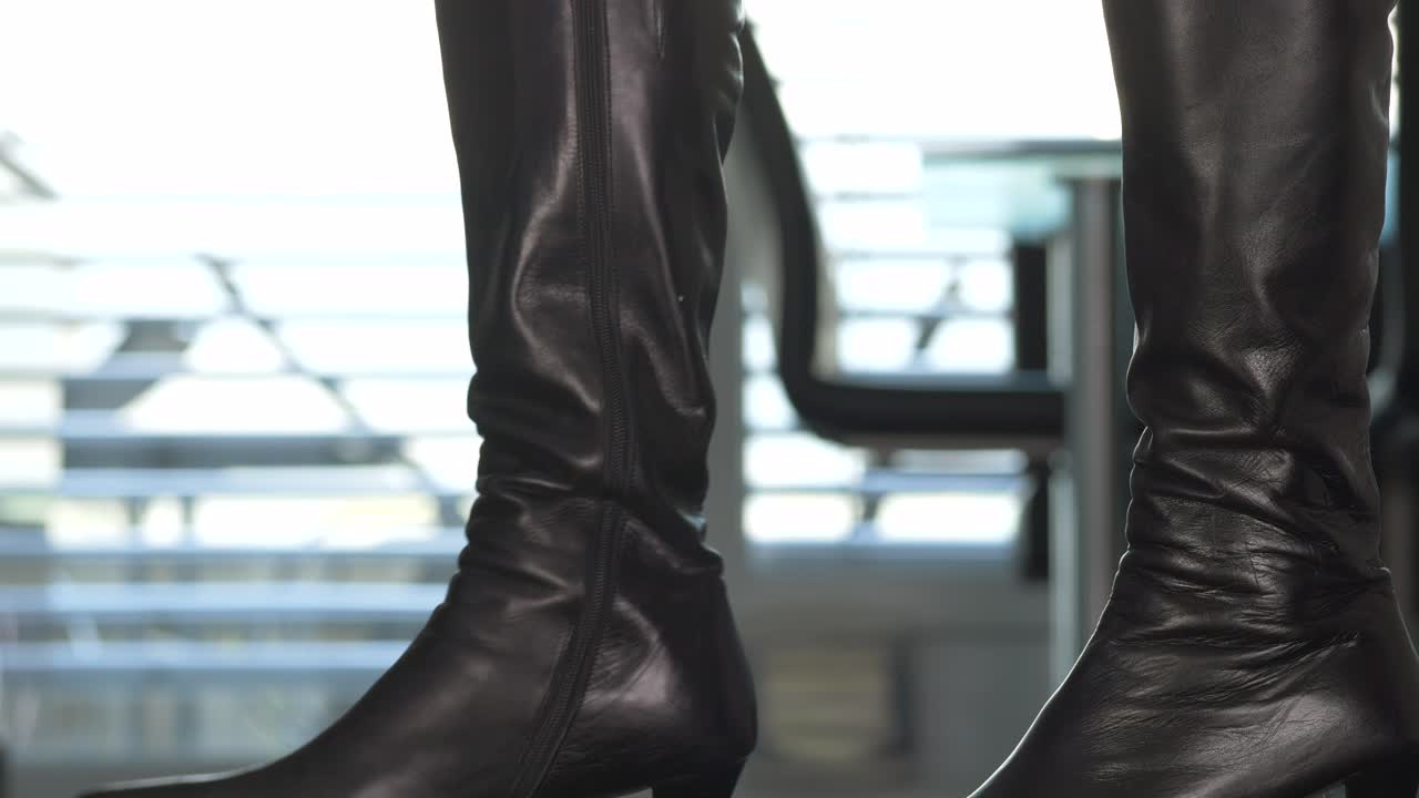 atractiva mujer deportiva con medias de nailon y botas de cuero con tacones golpeando nerviosamente el suelo