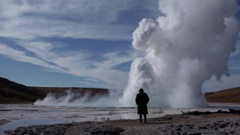 person observing a powerful geyser in a geothermal landscape