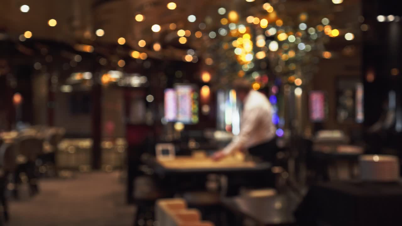 Croupier standing in front of poker table in casino, blurry interior pan left view