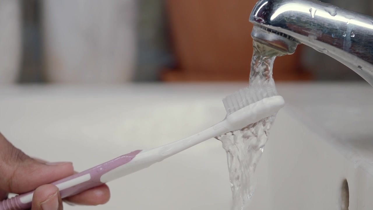 Persona enjuagando un cepillo de dientes bajo el agua corriente en el lavabo del baño
