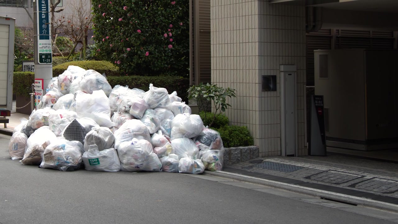 Inquadratura fissa di sacchi della spazzatura bianchi accumulati su un marciapiede a Tokyo, Giappone