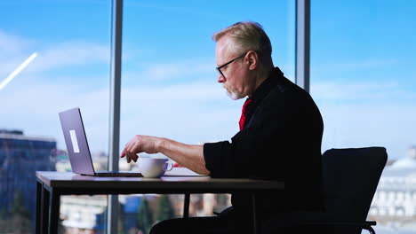 hard-working entrepreneur sits at desk working with papers. man types on laptop and checks info in his notes.
