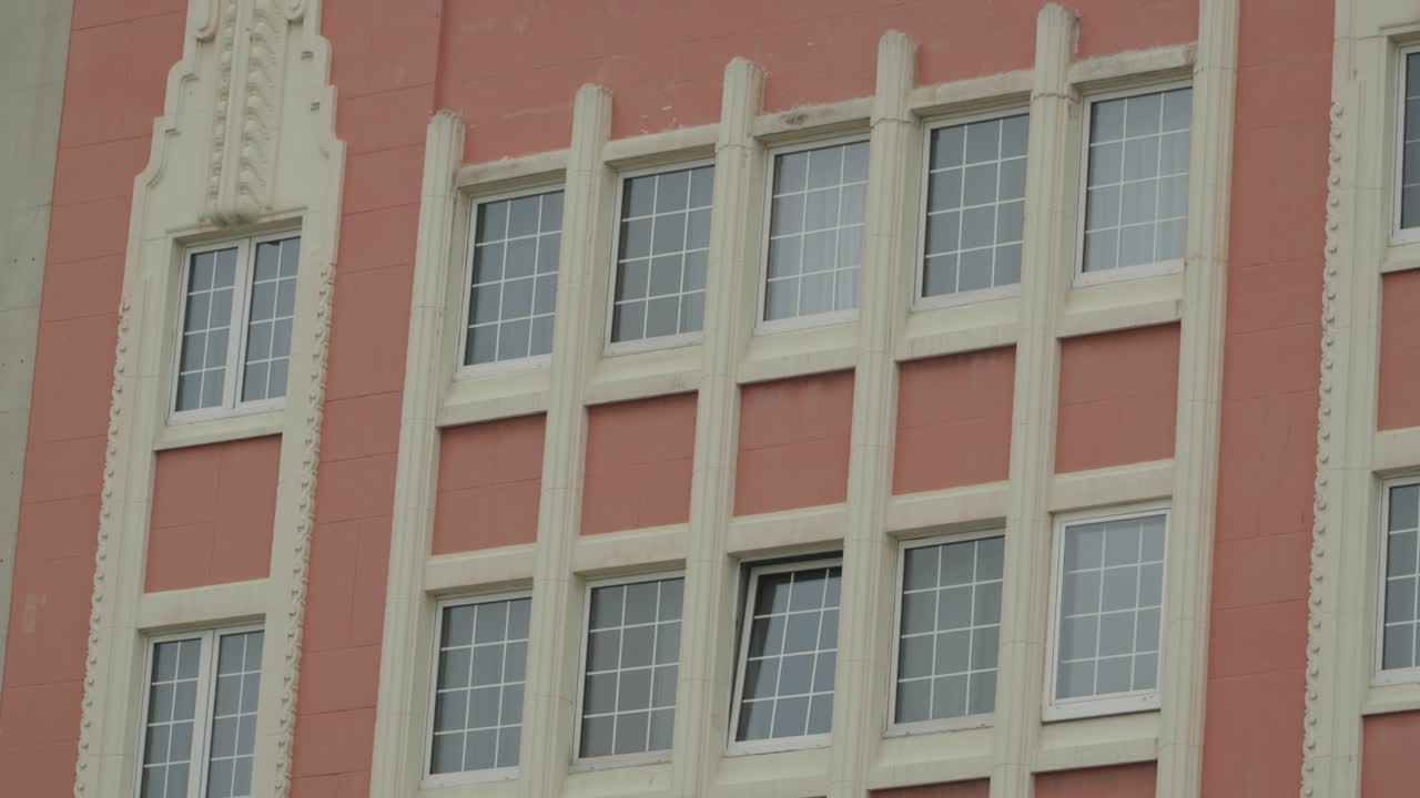 Primo piano dell'esterno di un classico edificio Art Déco a Gijón, Spagna, con colonne decorative bianche ornate e finestre a griglia simmetriche su una facciata rosa terracotta