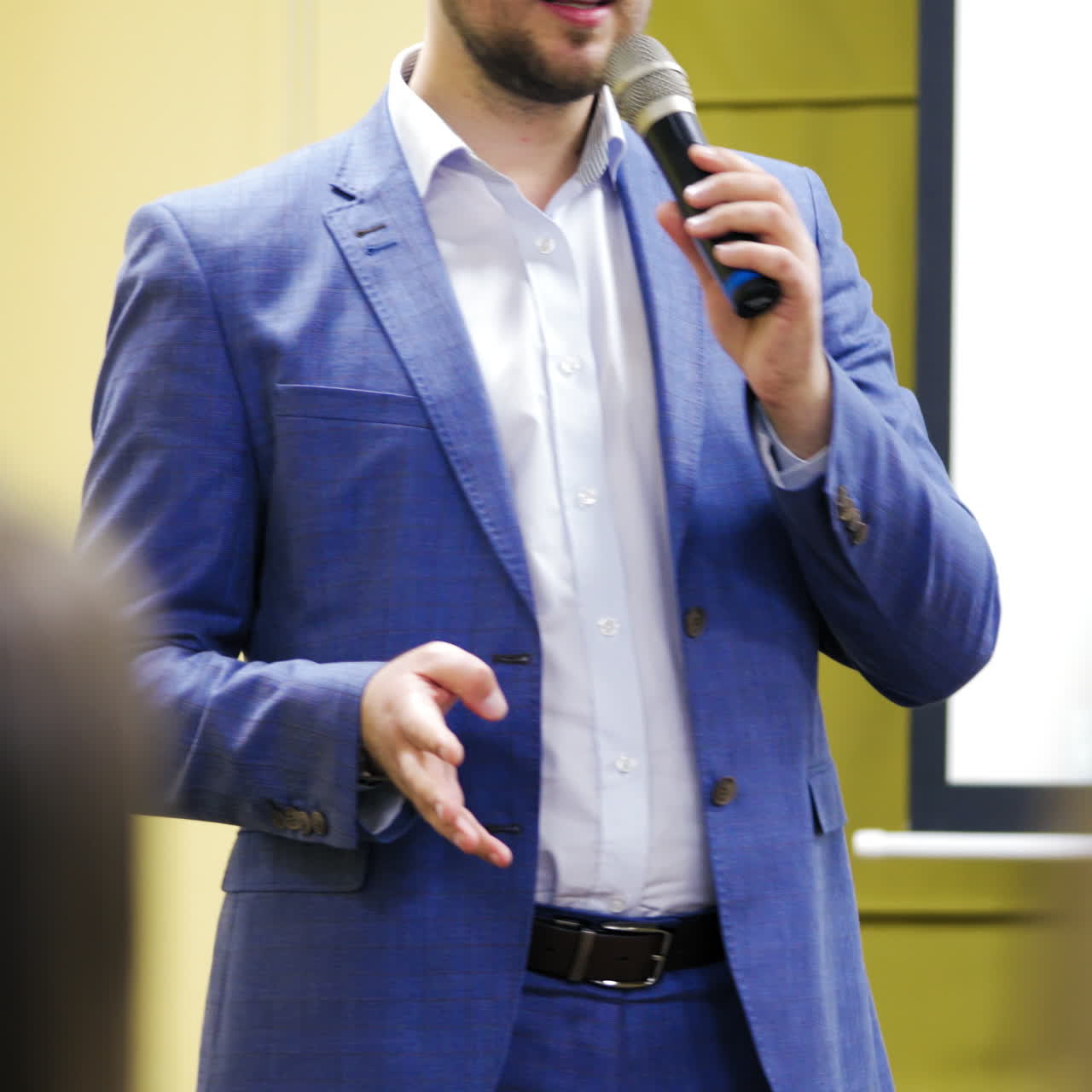 Man in blue suit is speaking in the conference hall gesticulating with his hand. Executive leader with a microphone and stylish clothes talking to people. Close-up.