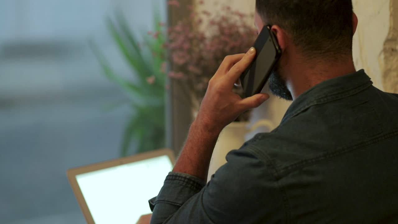 hombre usando teléfono celular y portátil en una cafetería