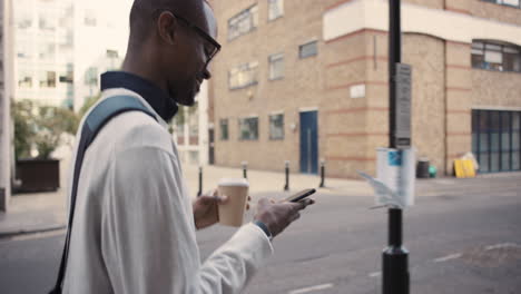 african american businessman walking through city using smart phone
