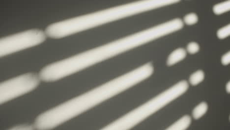 man passes his hand on the white wall with a hard window shadow from sun