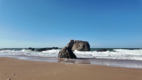 Waves-gently-crash-against-the-sandy-beach,-revealing-stunning-rock-formations-under-a-clear-blue-sky-in-Crimea-by-the-Sea-of-Azov