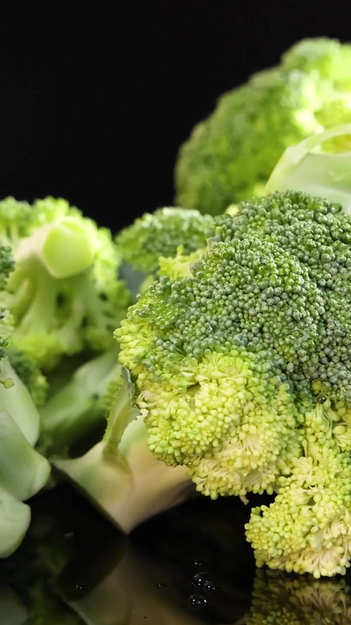 Scatto macro verticale di cimette di broccoli verde vibrante che ruotano su uno sfondo nero riflettente