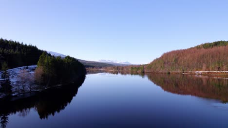 calm lake with perfect reflection of trees and distant mountains, no wind