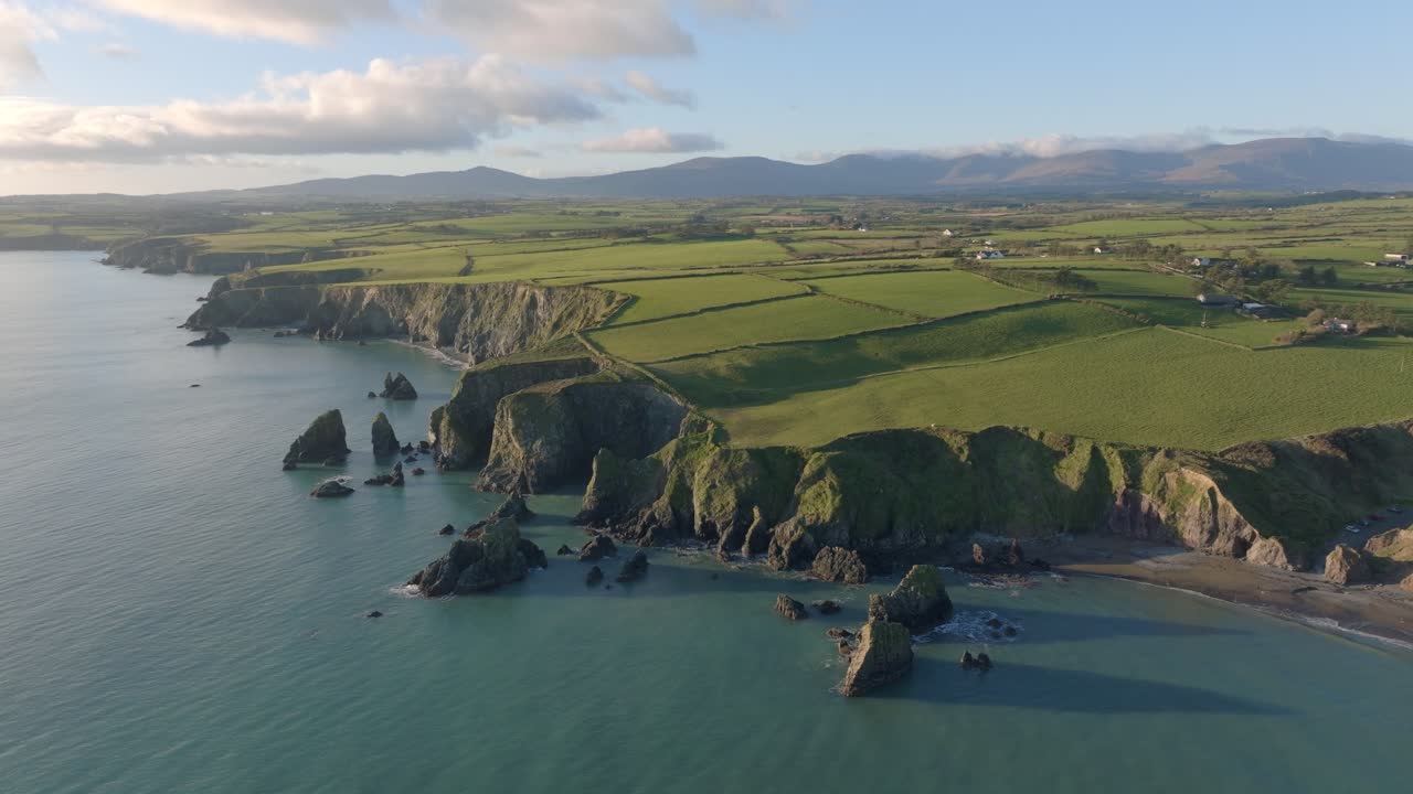 Dronelandskab med havstakke, strande, klipper, landbrugsjord og bjerge ved Copper Coast, Waterford, Irland