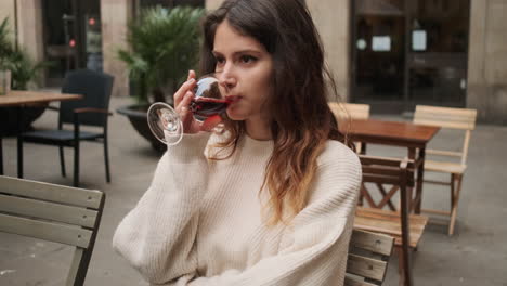 una joven sentada en un café bebiendo un vaso de vino tinto