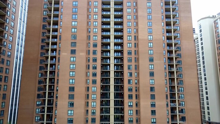 Vista frontale centrata di una facciata residenziale di media altezza con colonne di finestre verticali ripetitive, balconi incassati, ringhiere metalliche, superfici in mattoni di terracotta caldi, simmetria, texture e edilizia urbana