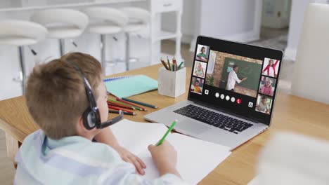 schoolboy using laptop for online lesson at home, with diverse teacher and class on screen