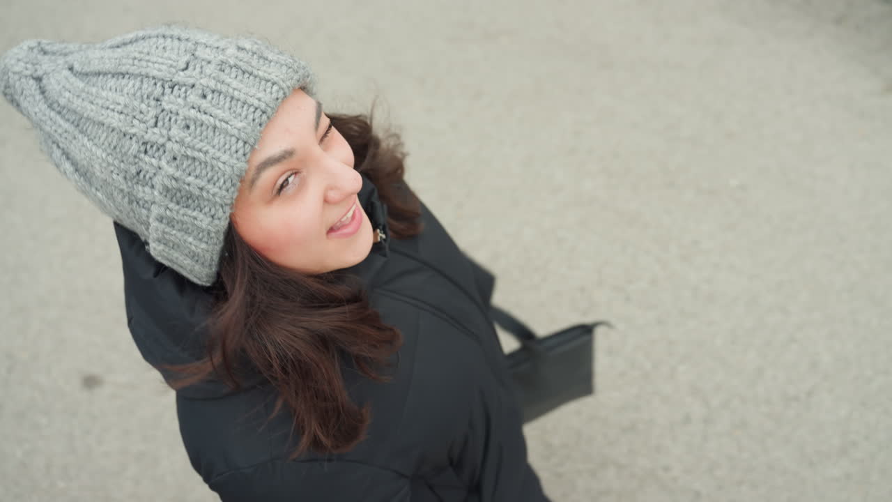 Mulher com casaco dançando de forma divertida ao ar livre. Mulher de gorro de malha exibindo expressões de dança animadas. Mulher casual de casaco preto flagrada no meio da dança com atitude energética e gesto divertido.