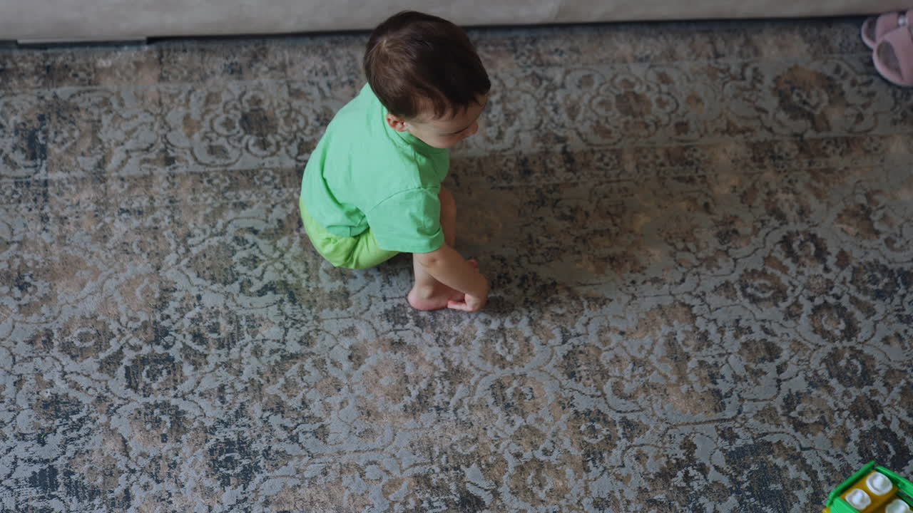 Lovely baby boy pushing his toy train by the carpet. Toddler plays at home. Top angle perspective.