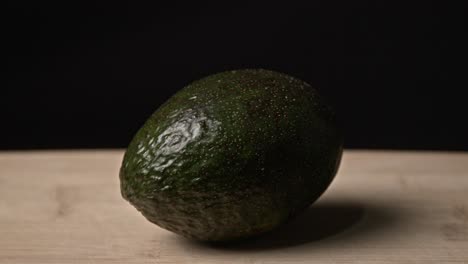 a ripe avocado sits on a rustic wooden table, softly lit in a low-light setting. the scene emphasizes natural textures and organic tones, creating a calm, minimalist atmosphere