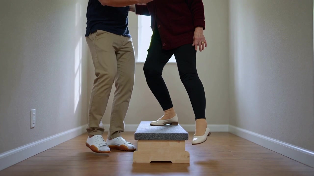 Lifting Senior woman cardigan placing right foot on step in hall, helper reaching steadying balance