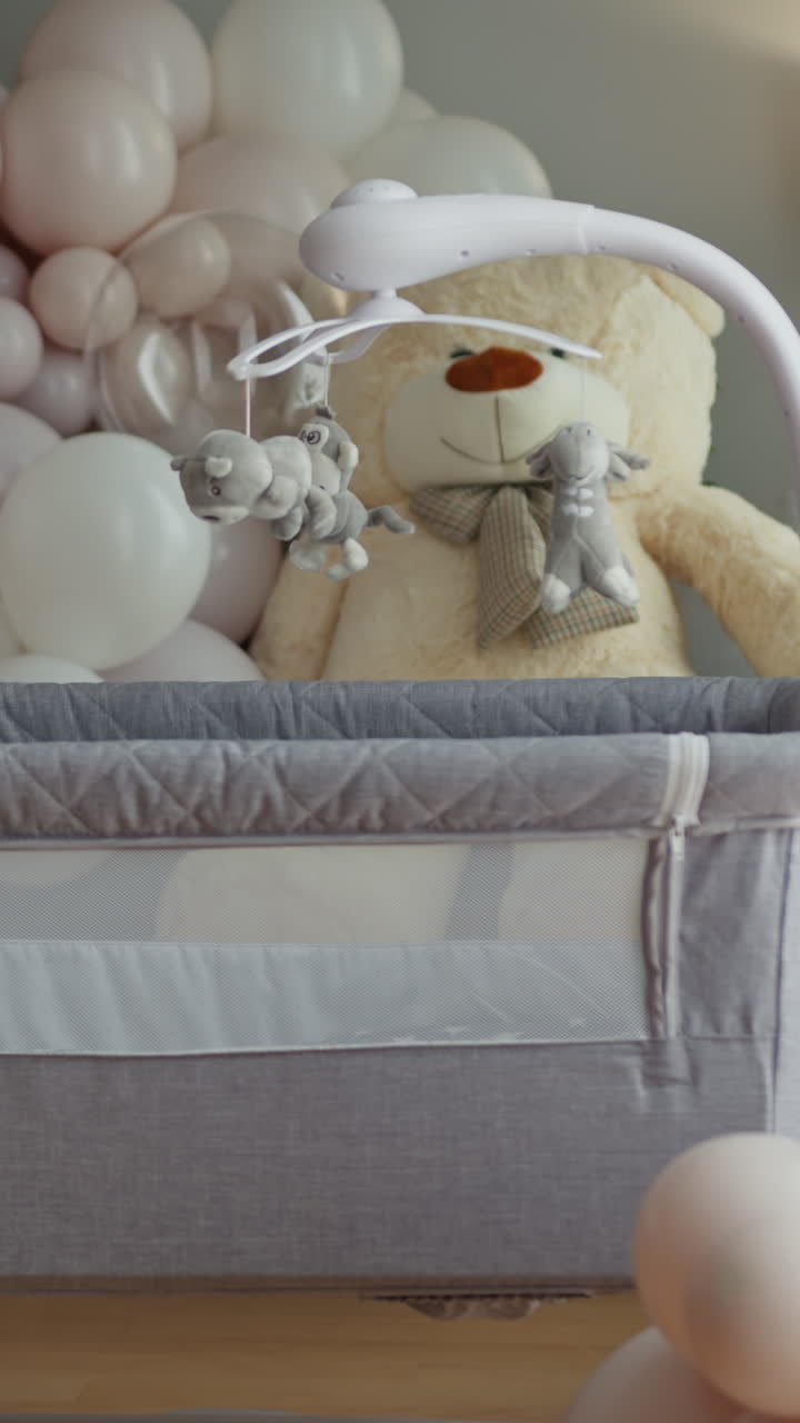 Un morbido orsetto di peluche e una giostrina di animali di peluche pendono sopra una culla circondati da palloncini pastello.