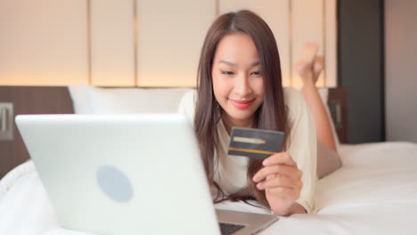 close-up of a pretty young woman lying on her stomach on the bed inputting her credit card number to a website