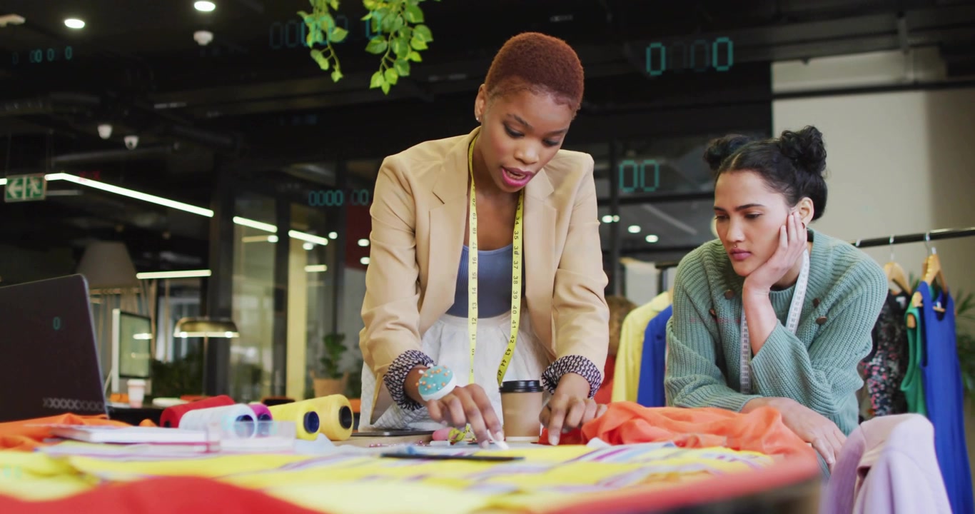 Fashion instructor unrolling orange fabric marking patterns while colleague watching for input