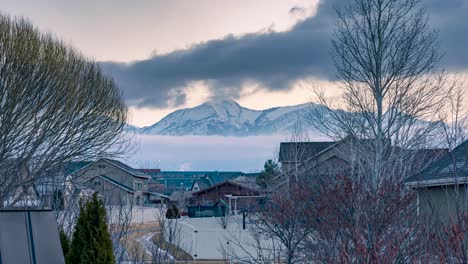 Vorstadtviertel-Mit-Wolken,-Die-Sich-In-Zwei-Schichten-In-Entgegengesetzte-Richtungen-Vor-Dem-Schneebedeckten-Berg-Bewegen-–-Zoomender-Zeitraffer