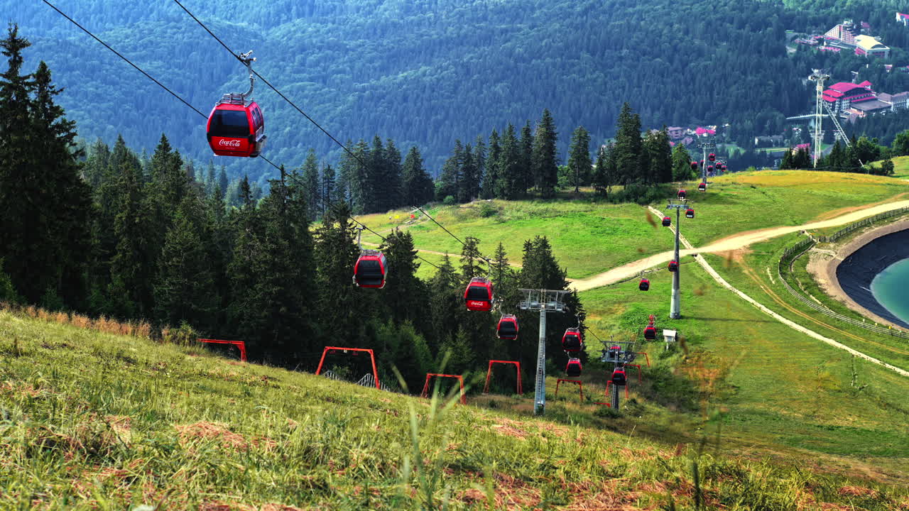 POIANA BRASOV, ROMANIA - AUGUST 27, 2023: View of moving cable cars on top of the mountain covered with lush forest