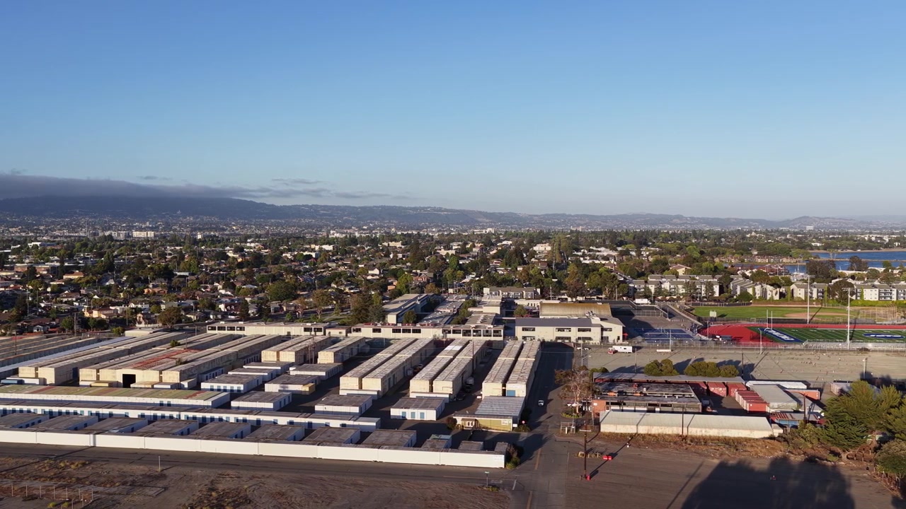 Une vidéo de drone panoramique capture West Alameda, Californie, avant le coucher du soleil en été. Les bâtiments industriels, les terrains de sport et les quartiers résidentiels brillent d'une lumière dorée et chaude vue d'en haut.