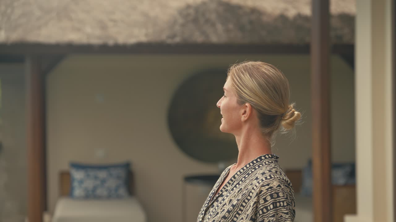 Donna bionda elegante, sicura di sé e di classe cammina fuori da una lussuosa villa tropicale in legno e si guarda intorno.