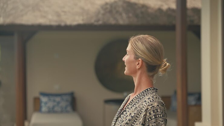 Donna bionda elegante, sicura di sé e di classe cammina fuori da una lussuosa villa tropicale in legno e si guarda intorno.