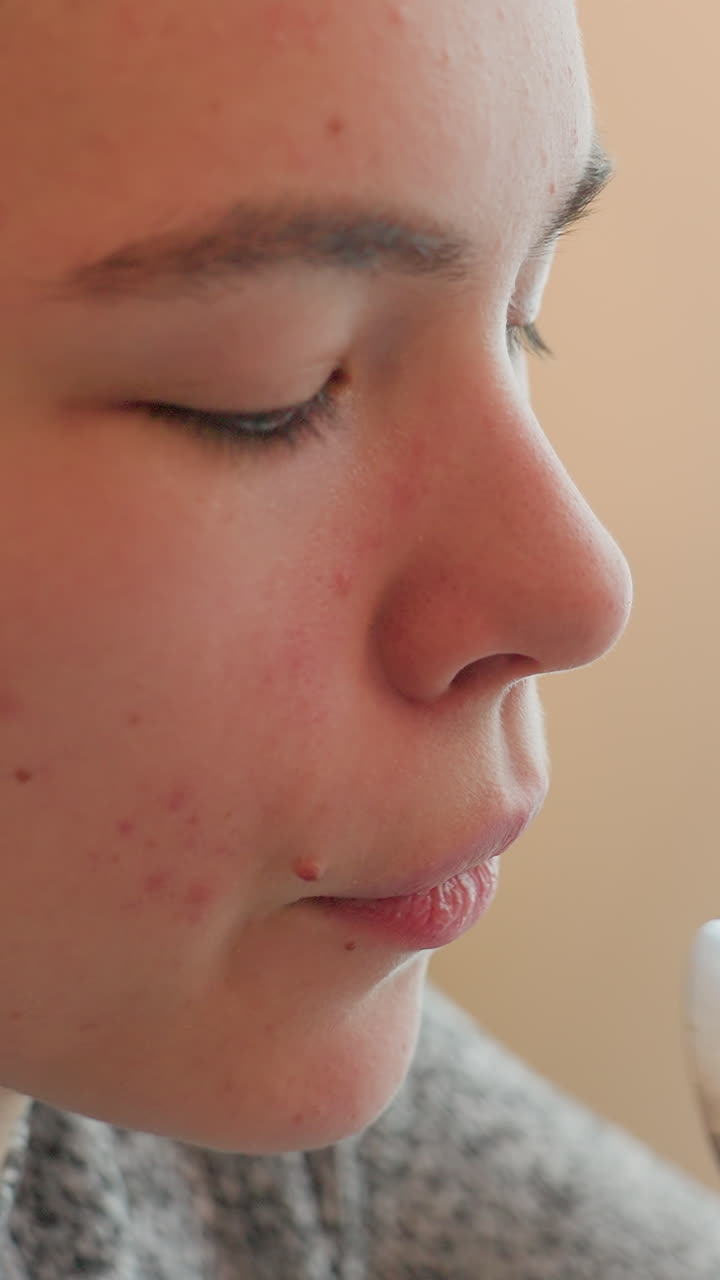 primo piano di un'adolescente bianca che assaggia con un cucchiaio, mostrando curiosità giocosa al tavolo, luce naturale calda, leggero contatto con le labbra, un po' di acne, profilo riflesso, cucchiaio in acciaio inossidabile, scena di uno spuntino domestico, cuoco casalingo che assaggia