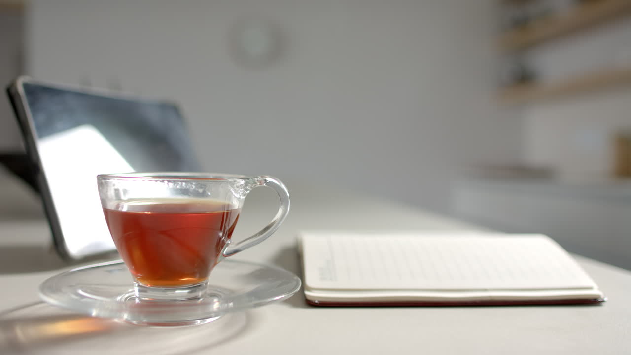 A cup of tea sits on saucer next to open notebook on a desk
