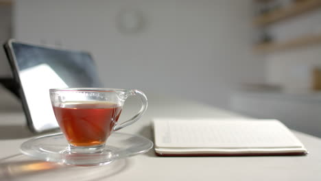a cup of tea sits on saucer next to open notebook on a desk