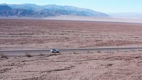 Aerial-view-of-car-driving-on-a-highway-through-beautiful-desert-scenery-in-Death-Valley,-California,-US