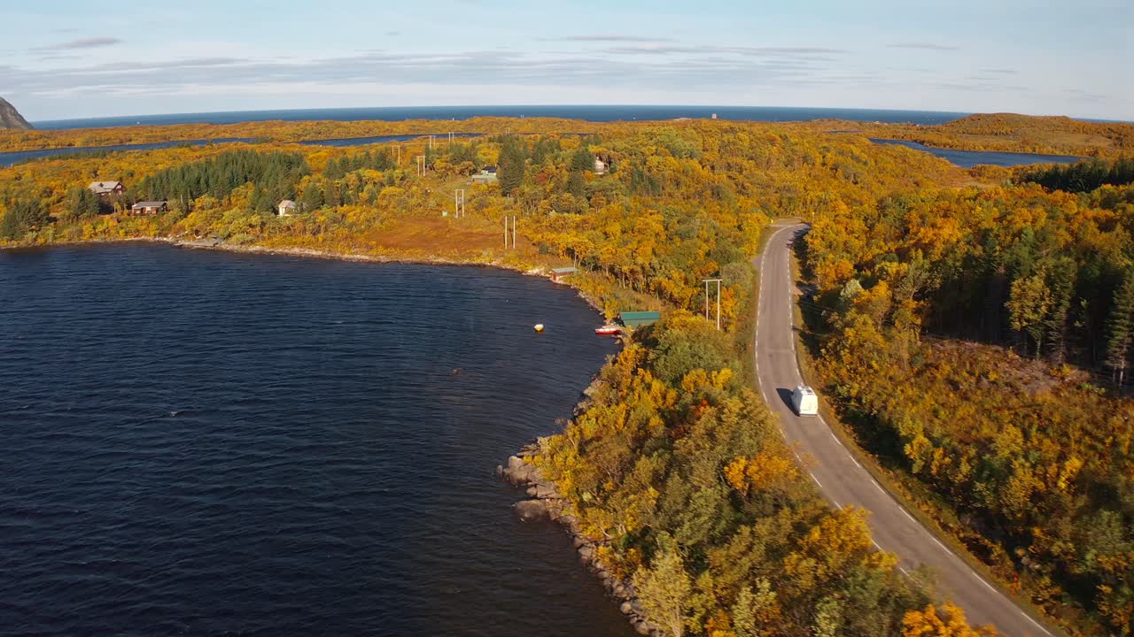 A winding road along a lake in vestarelen, surrounded by autumn trees, aerial view